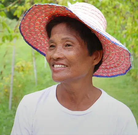 Une agricultrice avec un chapeau de paille sourit en nous regardant